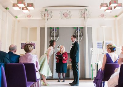 Wedding ceremony in the music room of House For An Art Lover, bride wearing green tea dress